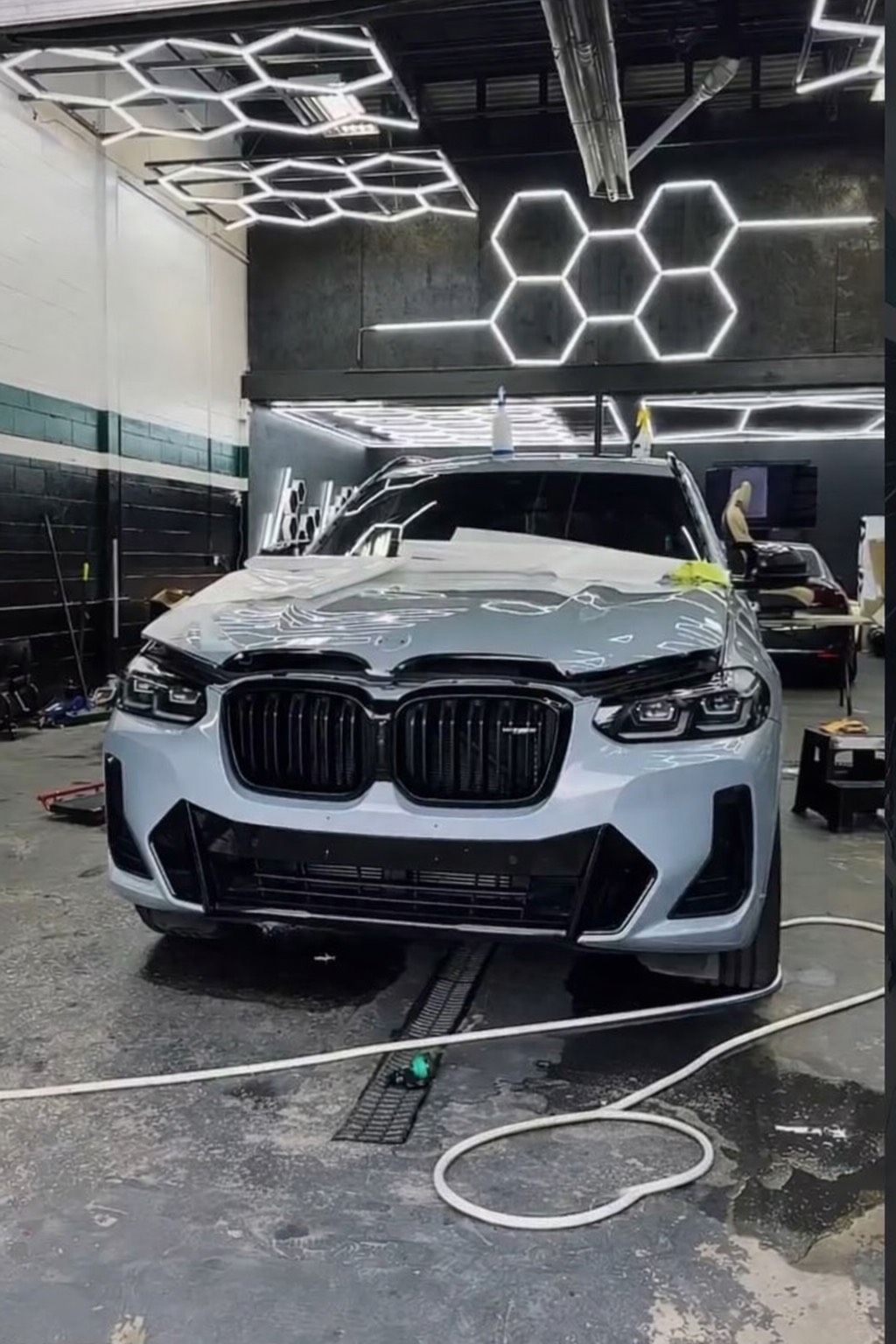 Silver sports car in a PPF installation bay with wrap films on the wall